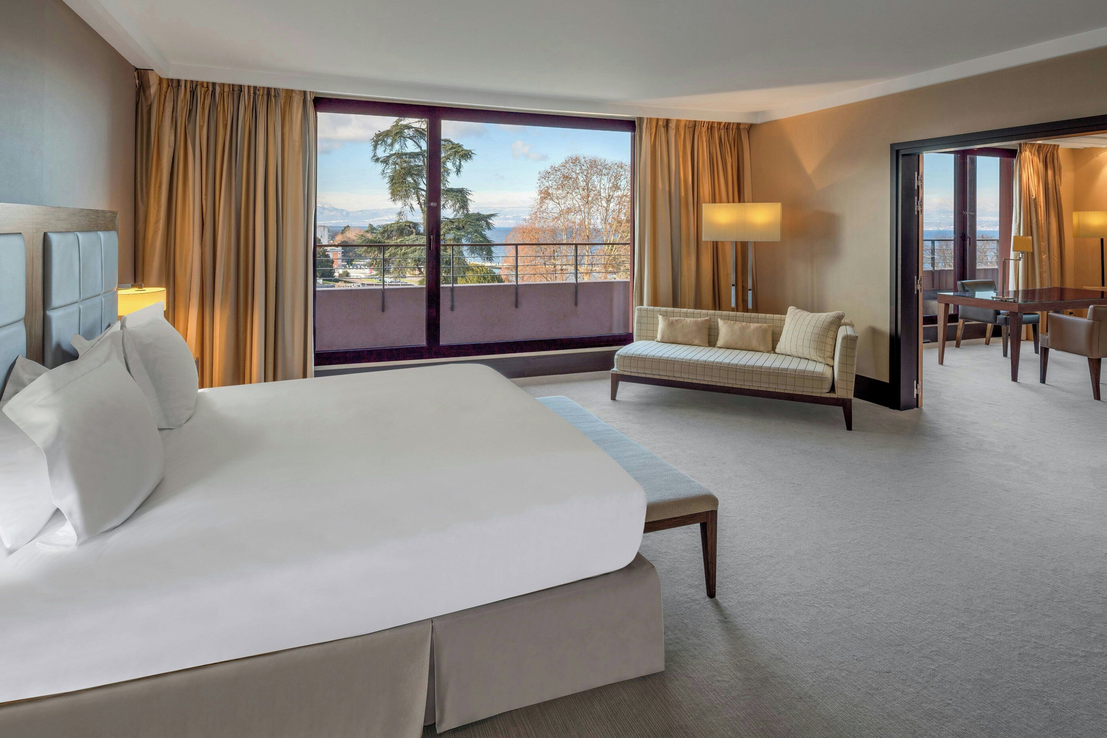 Habitación de hotel con una cama grande, un sofá, una mesa de comedor y vistas al exterior.