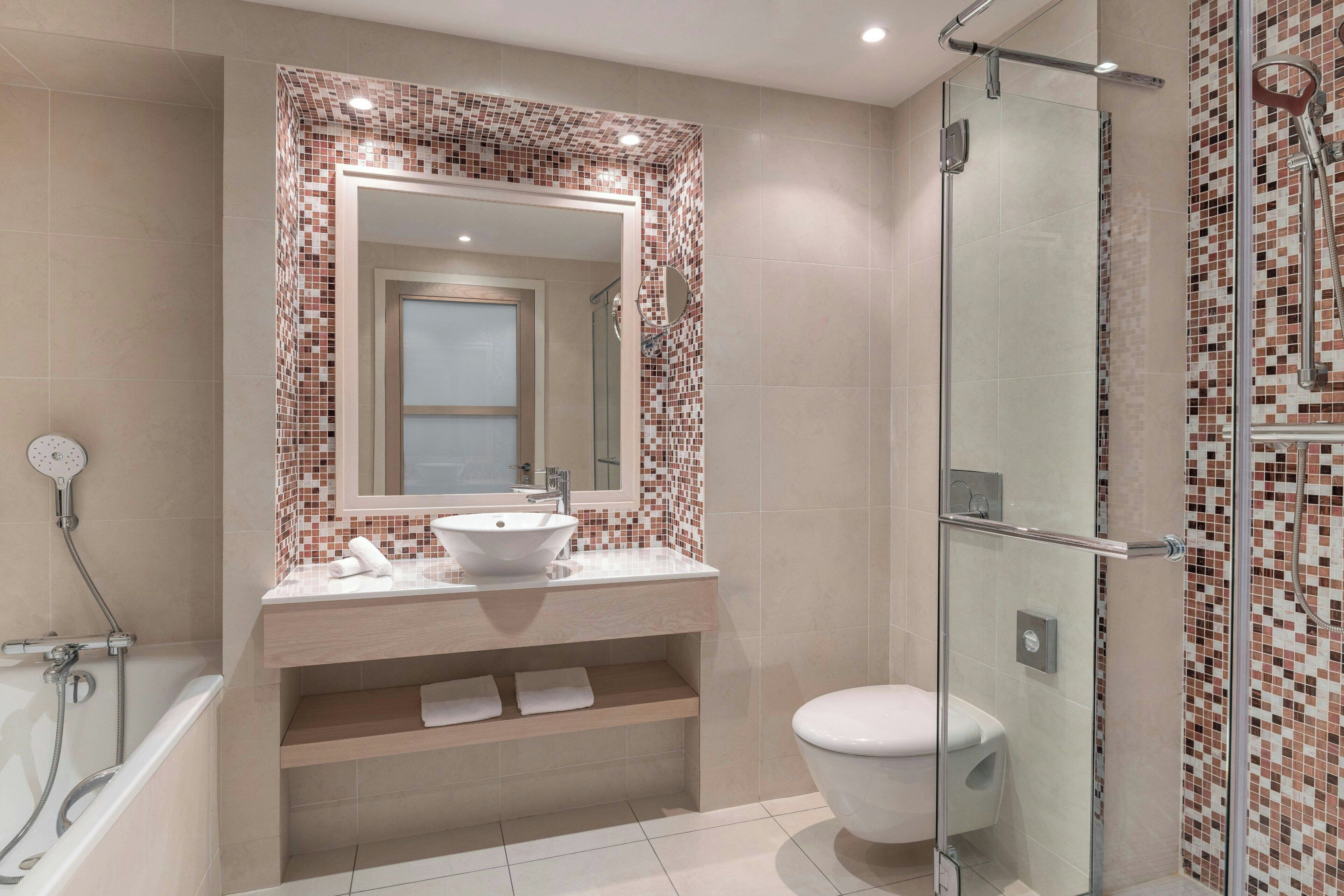Un baño moderno con cabina de ducha de vidrio, un lavamanos blanco con un espejo encima y una bañera.