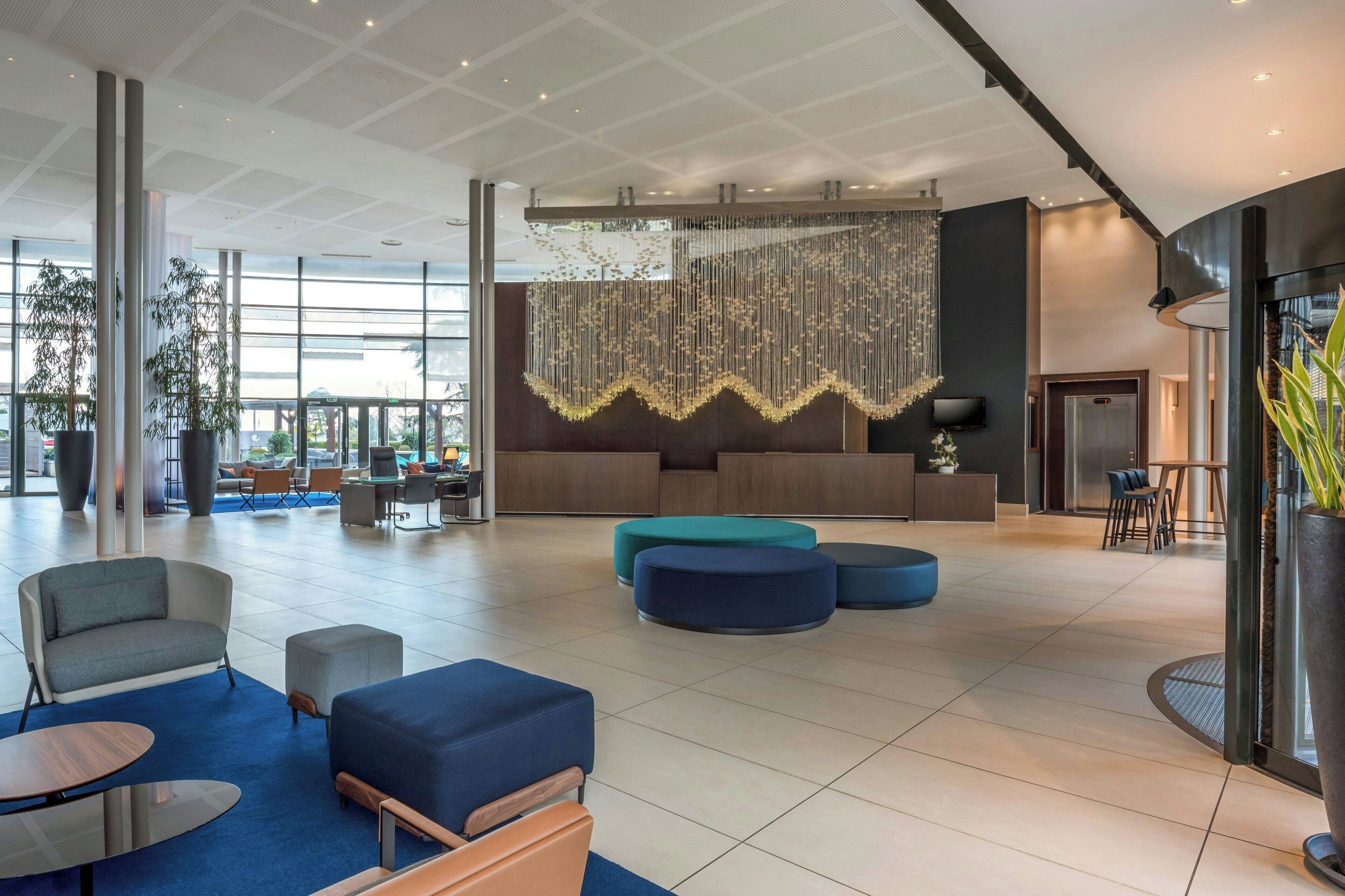 Un lobby amplio con mobiliario moderno, una lámpara de araña grande y una mesa de recepción.