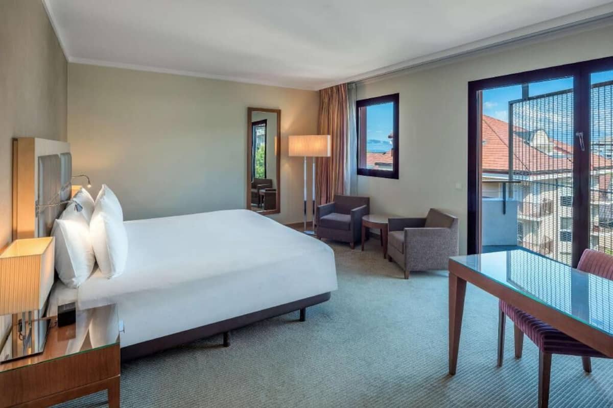 Une chambre d’hôtel équipée d’un lit, d’un bureau, d’une chaise, d’une lampe et d’une grande fenêtre donnant sur un beau paysage.