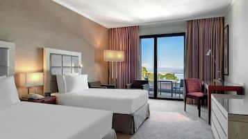 Ein Hotelzimmer mit zwei Betten, einem Schreibtisch, einem Stuhl, einer Lampe und Blick ins Freie.