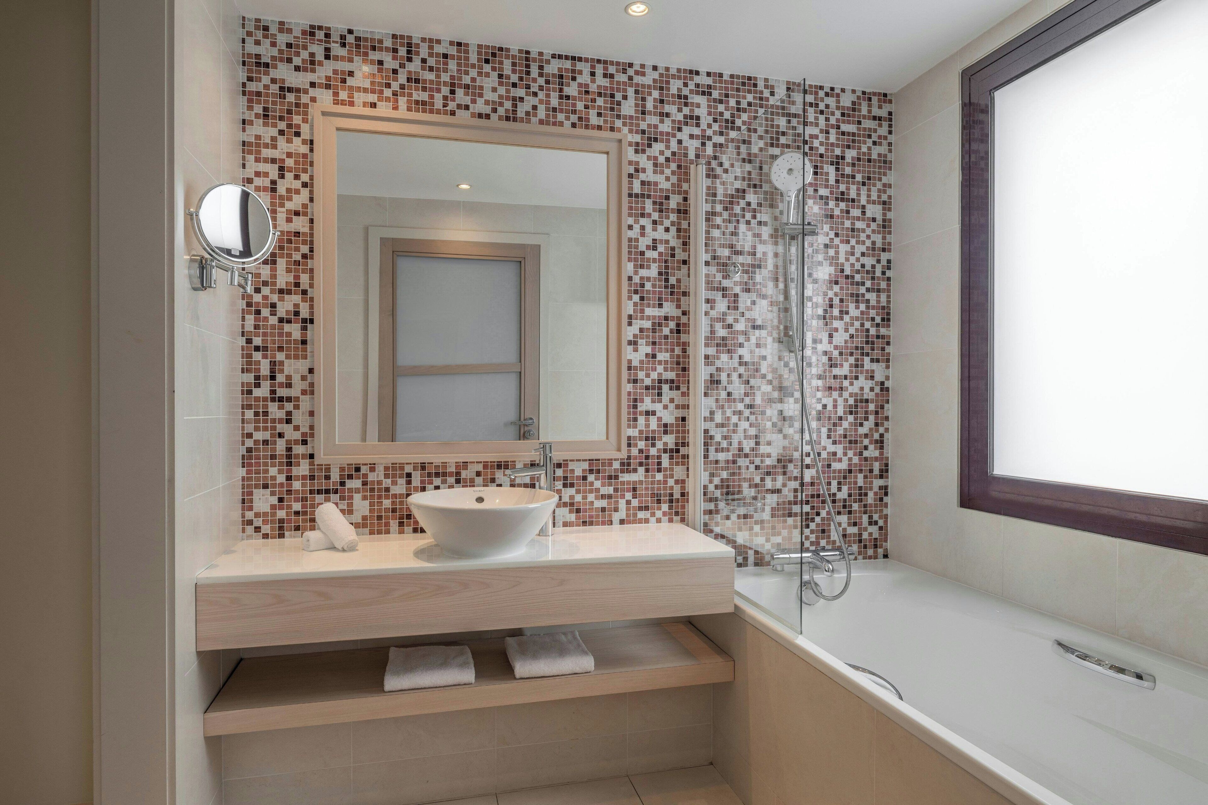 Un baño moderno con un espejo grande, un lavamanos sobre encimera, cabina de ducha y ventana.