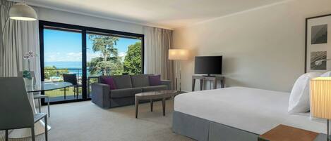 Une chambre d’hôtel équipée d’un lit, d’un bureau, d’un canapé, d’une télévision et d’un balcon donnant sur l’extérieur.