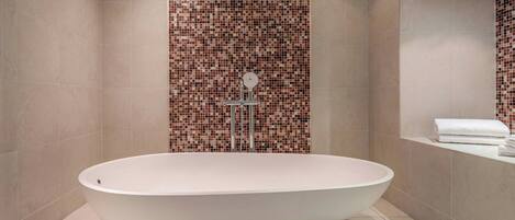 Un baño moderno con una bañera independiente, un muro de ducha con azulejos y una toalla blanca en un estante.