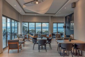 A spacious indoor area with multiple seating arrangements, large windows offering a view of the outdoors, and a modern ceiling design. - Hotel Evian-les-Bains by Leonardo Hotels (Evian-les-Bains)