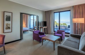 A hotel room with a balcony, a TV, purple and grey furniture, and a large window with curtains. - Hotel Evian-les-Bains by Leonardo Hotels (Evian-les-Bains)