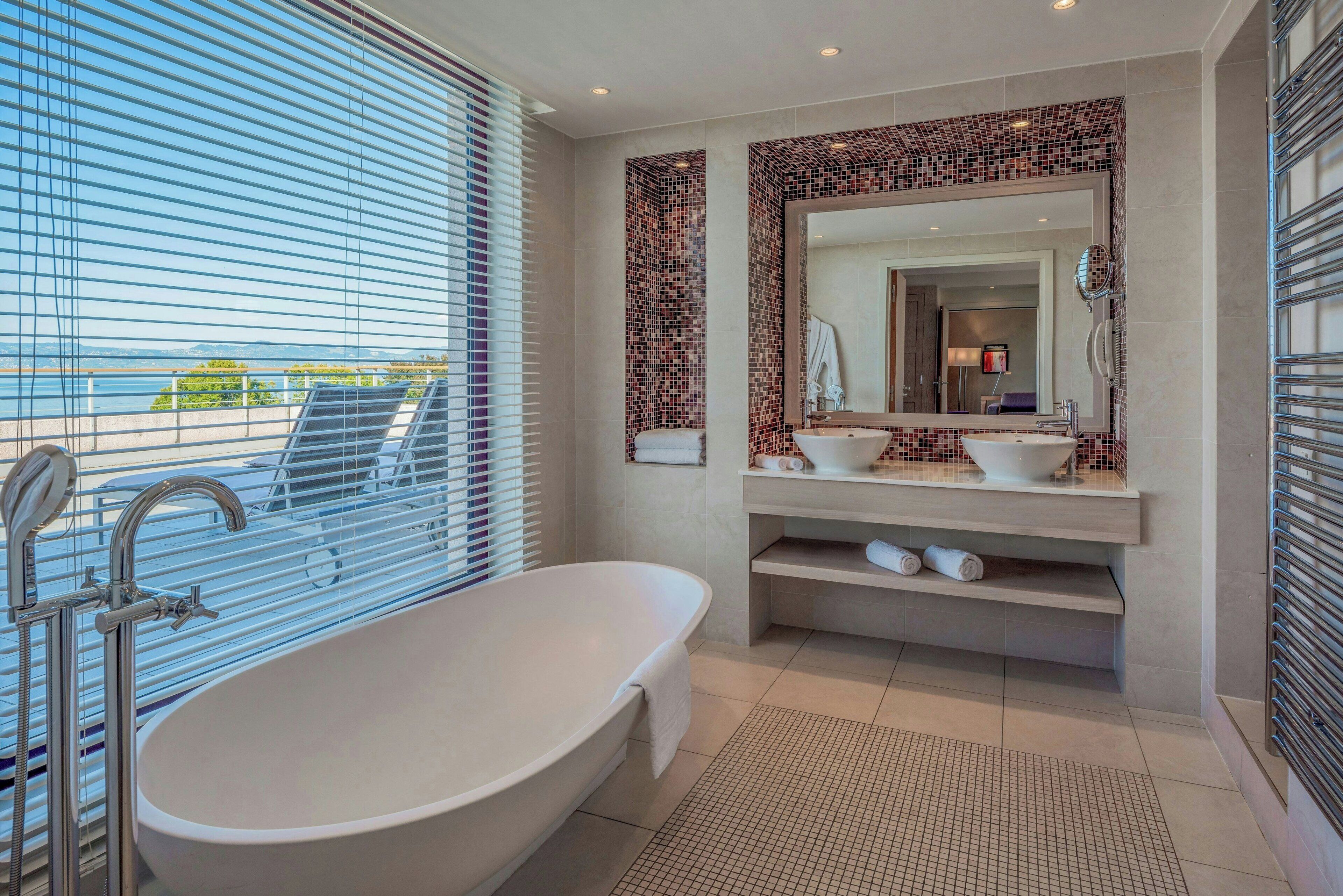 Une salle de bain moderne avec une baignoire sur pieds, un grand miroir et un mur recouvert de carreaux.