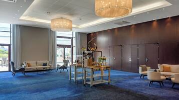 Un hall d’hôtel avec un tapis bleu, des espaces aménagés avec des sièges, un comptoir d’accueil et une grande fenêtre.