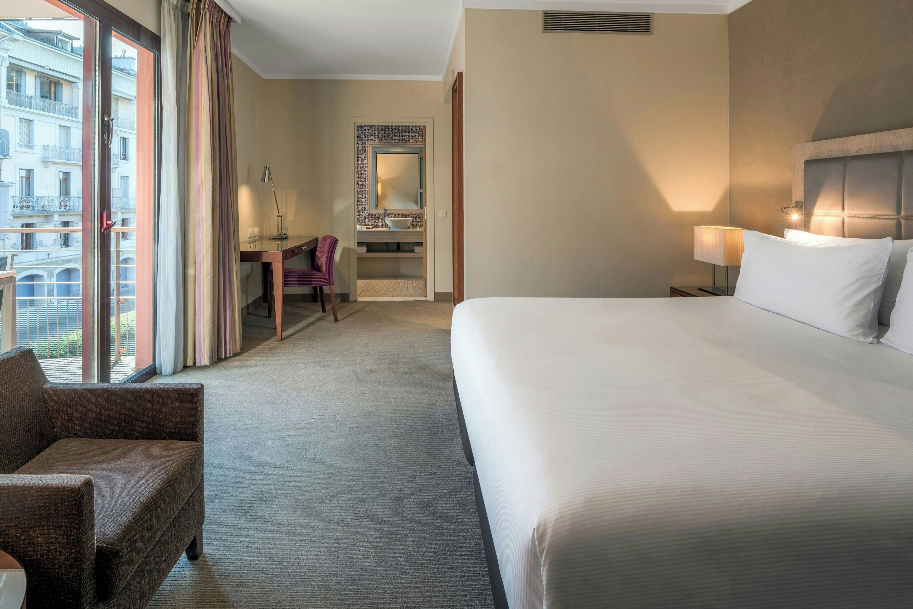 Habitación de hotel con una cama grande, un escritorio con una silla, un baño con espejo y vistas a la ciudad desde la ventana.