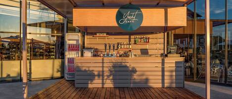 Un pequeño bar al aire libre con mostrador de madera, refrigerador de Coca-Cola y una variedad de botellas.