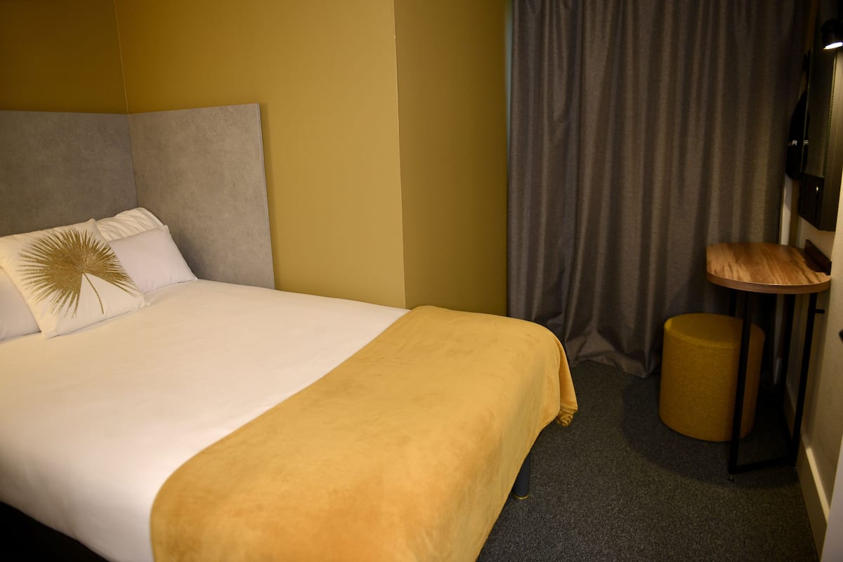 Una habitación de hotel con una cama, una mesita de noche, una lámpara y una cortina.