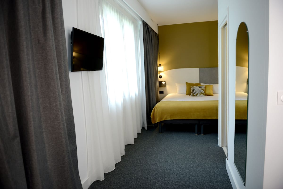 Habitación de hotel con cama, televisor, mesita de noche y ventana con cortinas.