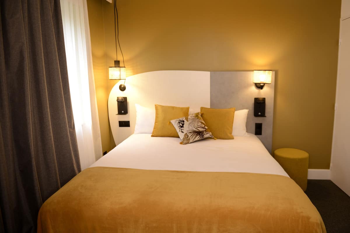 Una habitación de hotel con una cama grande, dos lámparas adosadas a la pared y una pequeña mesa redonda.