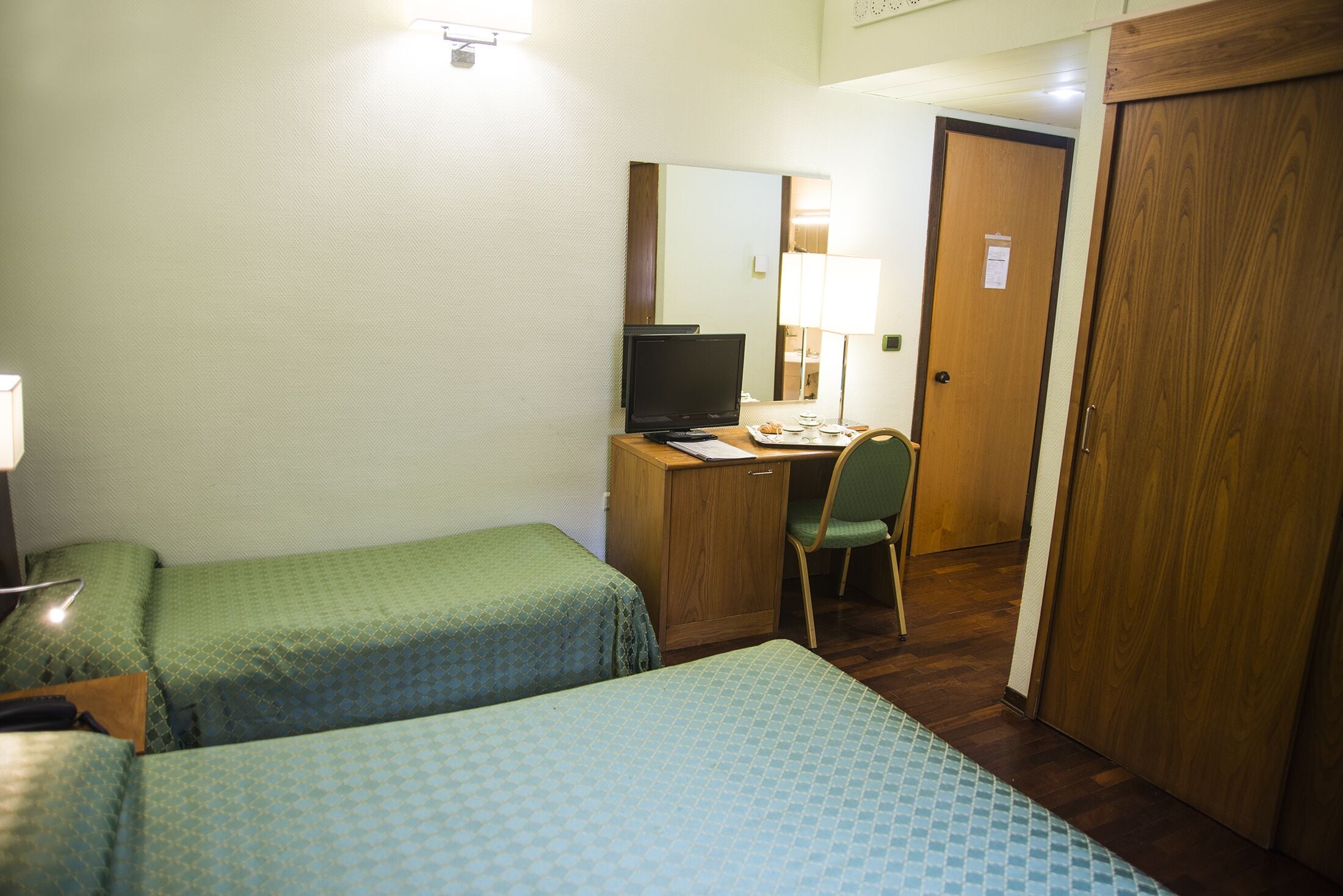Ett hotellrum med två sängar, ett skrivbord med en dator, en stol och en garderob i trä.