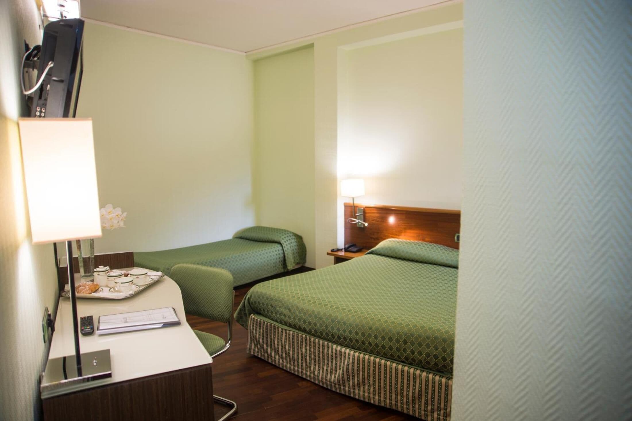 Una habitación de hotel con escritorio, dos camas individuales, una mesita de noche y una lámpara.