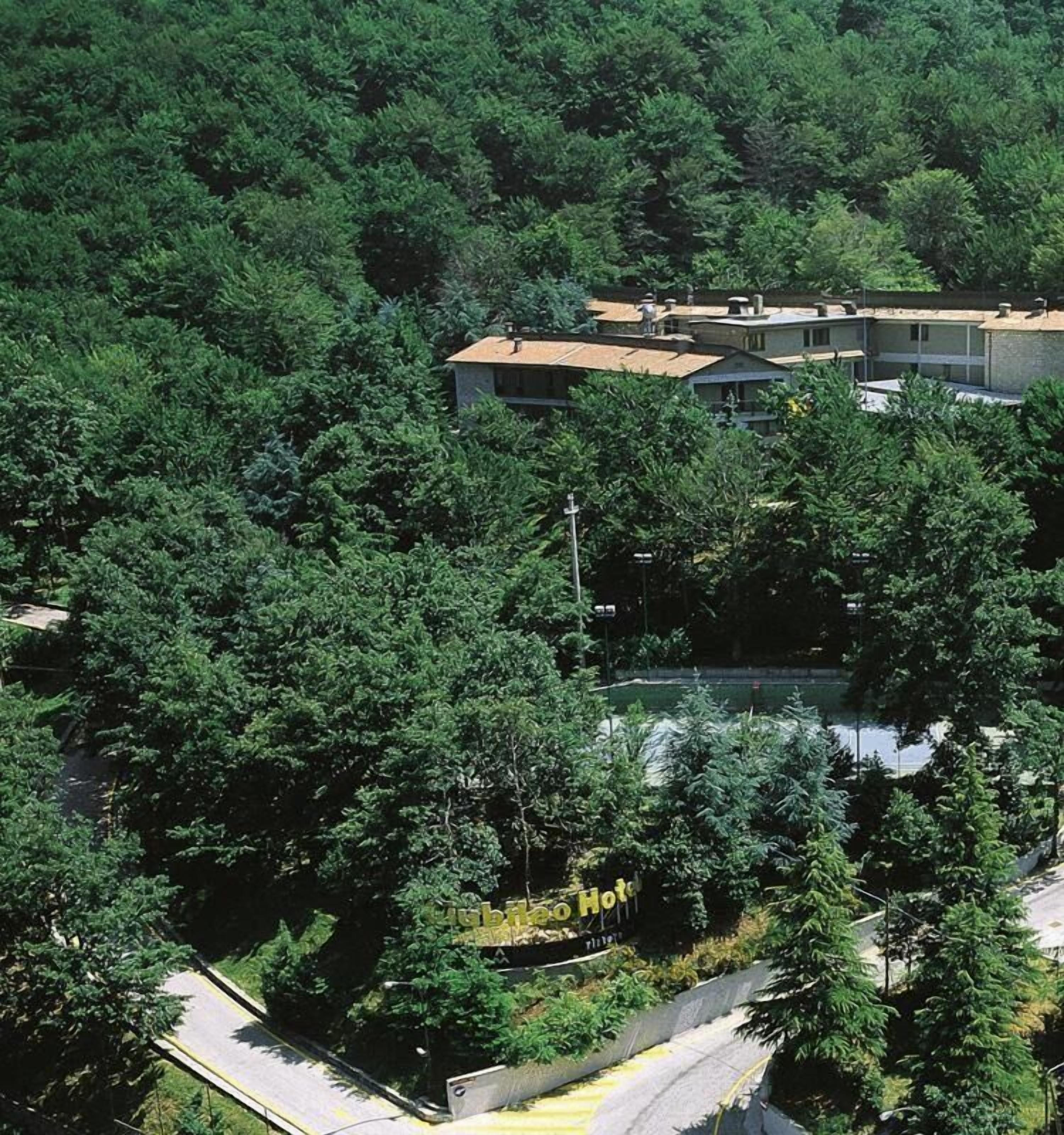Hotel rodeado de bosque denso, con piscina visible y un cartel que indica que es un hotel.