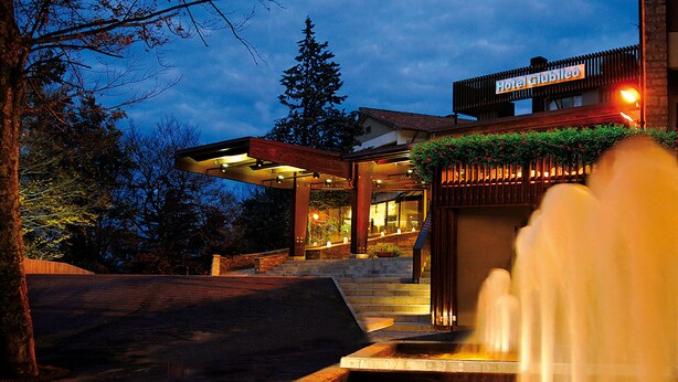 A modern hotel entrance with a well-lit facade, a visible staircase, and a water feature in the foreground. - Hotel Giubileo (Pignola)