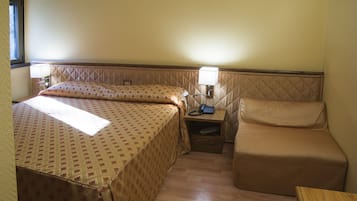 Ein kleines, gemütliches Hotelzimmer mit Bett, Nachttisch mit Lampe und Sessel.