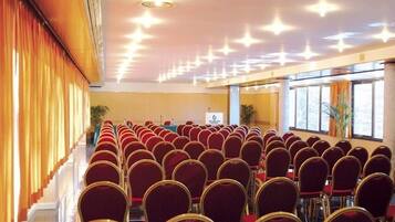 Una sala conferenze con file di sedie rosse e un palco con un podio.