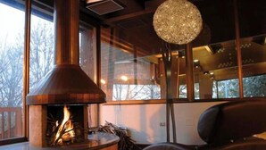 A modern interior with a wood-burning stove, large windows, and a round chandelier. - Hotel Giubileo (Pignola)