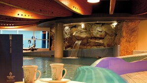 A spa area with a hot tub, a waterfall feature, and two cups on a table. - Hotel Giubileo (Pignola)