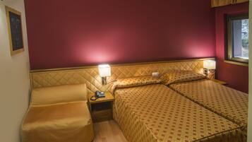 Ein Hotelzimmer mit Bett, Sessel, Nachttisch mit Lampe und Fenster.