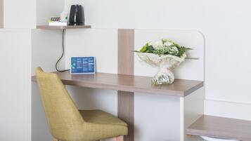 Un espace de bureau moderne comprenant un bureau, une chaise, une tasse de café, un vase avec des fleurs et un panneau accroché au mur.