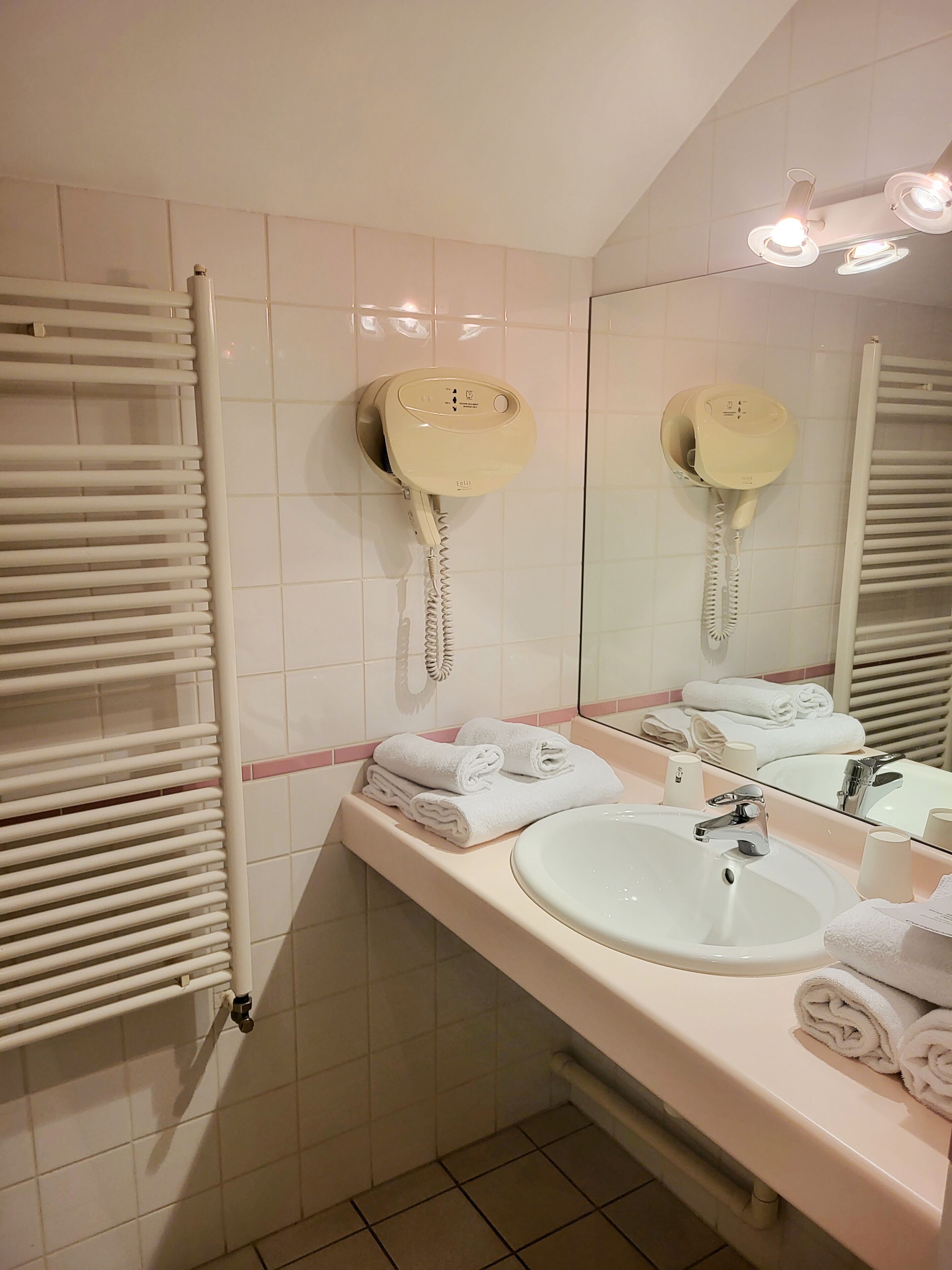 Un baño con un lavamanos blanco, un espejo y un perchero para toallas.
