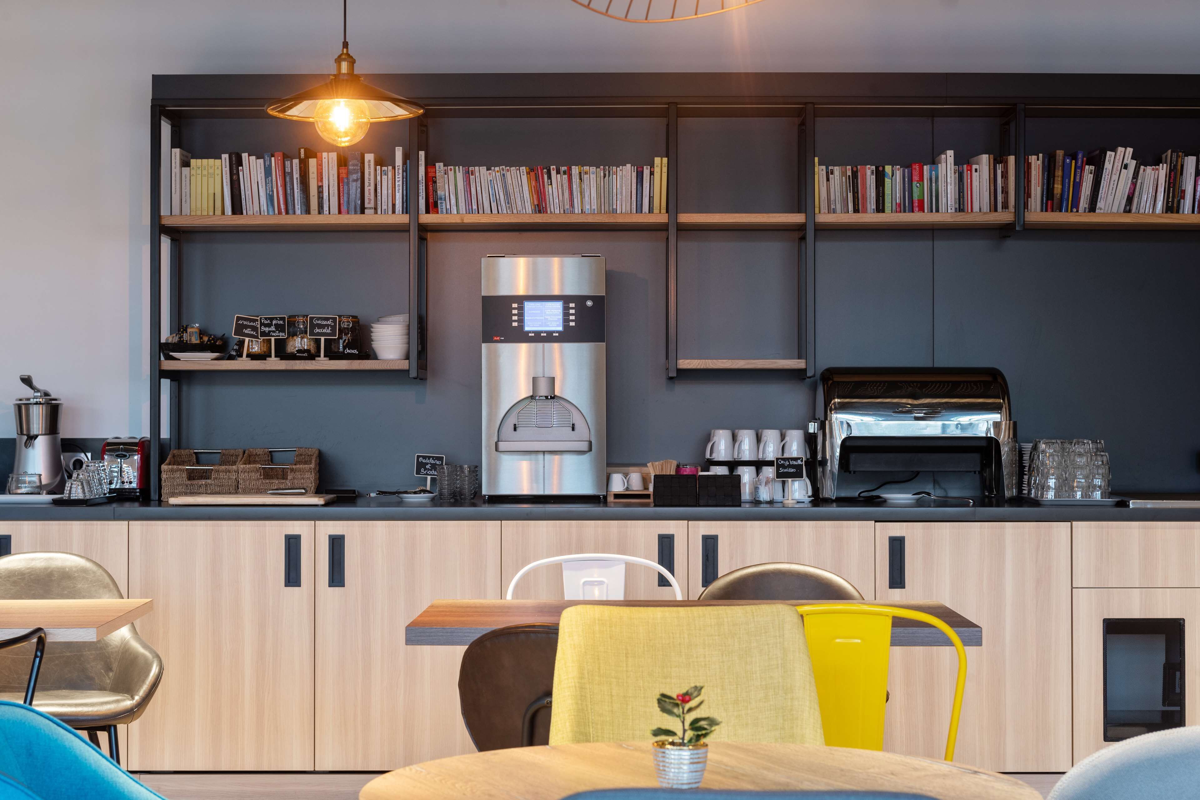 A modern kitchen with a coffee machine, a toaster, and a bookshelf filled with books.