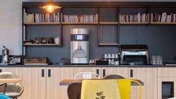 A modern kitchen with a coffee machine, a toaster, and a bookshelf filled with books.