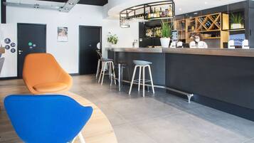 Un espace bar moderne avec un comptoir incurvé, des tabourets de bar et un coin salon comprenant une chaise bleue et une chaise orange.
