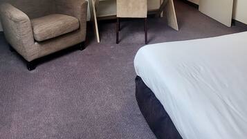 A hotel room with a bed, a desk with a chair, a sofa, a TV mounted on the wall, and an air conditioning unit.