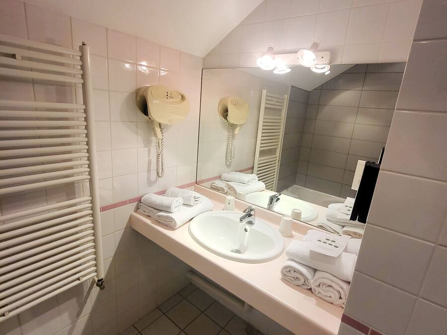 Un baño con un lavabo blanco, dos teléfonos fijos en la pared, un perchero para toallas y un espejo con iluminación.