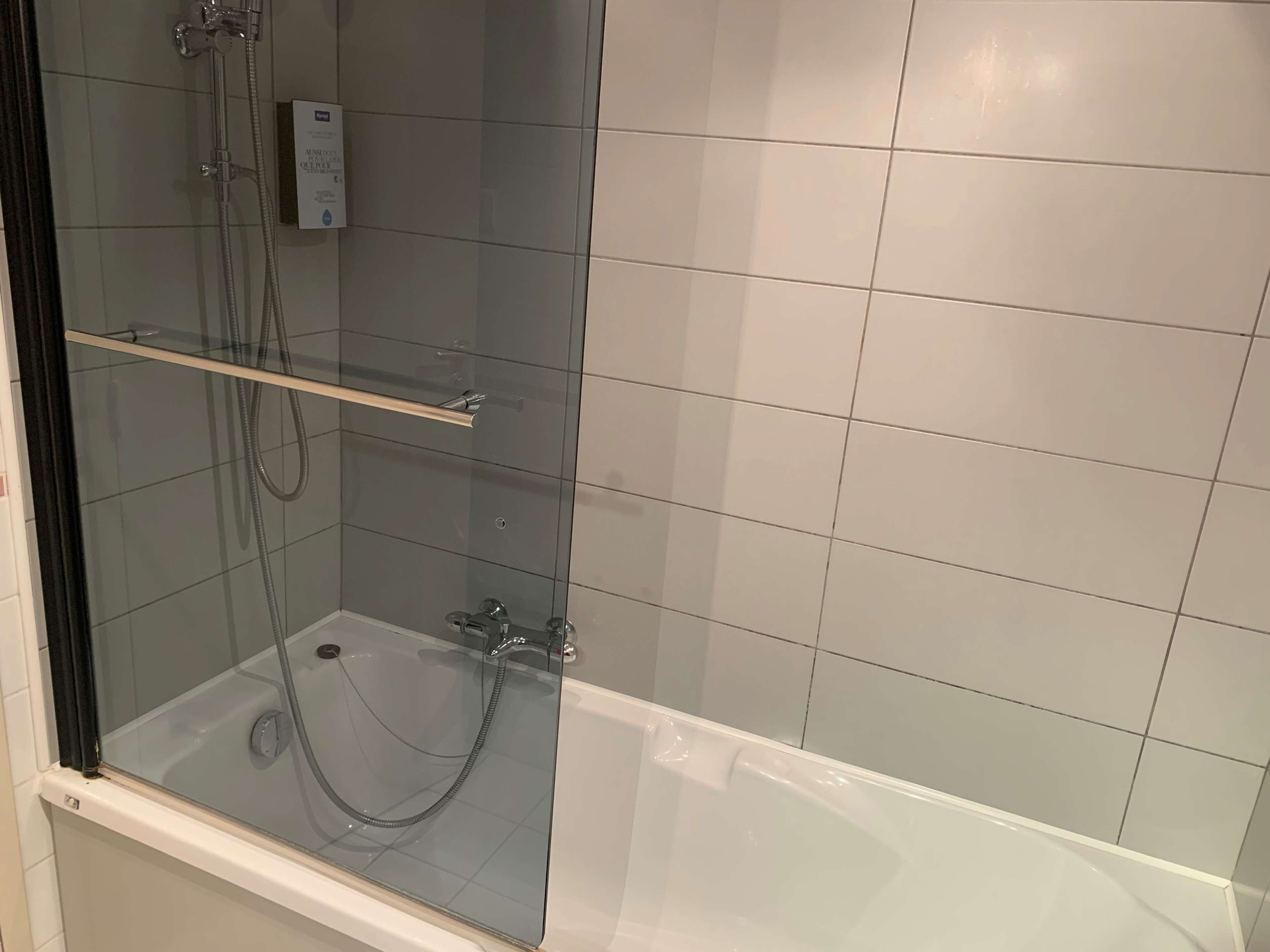 Un espace douche fermé par des parois de verre, avec une baignoire, une étagère en verre et un panneau de commande.