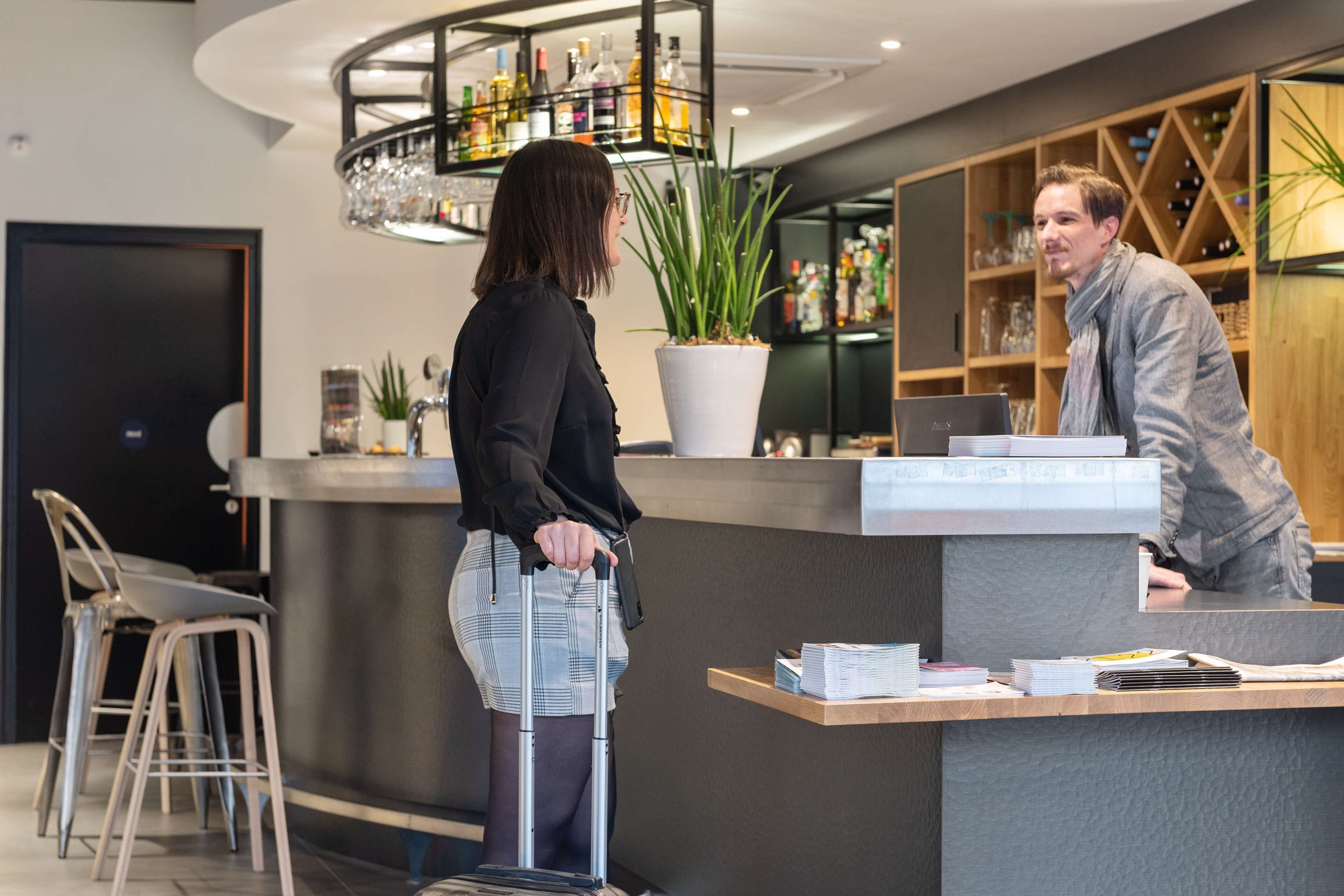 A reception area with a counter, bar stools, a potted plant, and a chandelier.