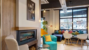 A modern living room with a fireplace, comfortable seating, and large windows offering a view of the city. - Campanile Epinal Centre - Gare (Epinal)