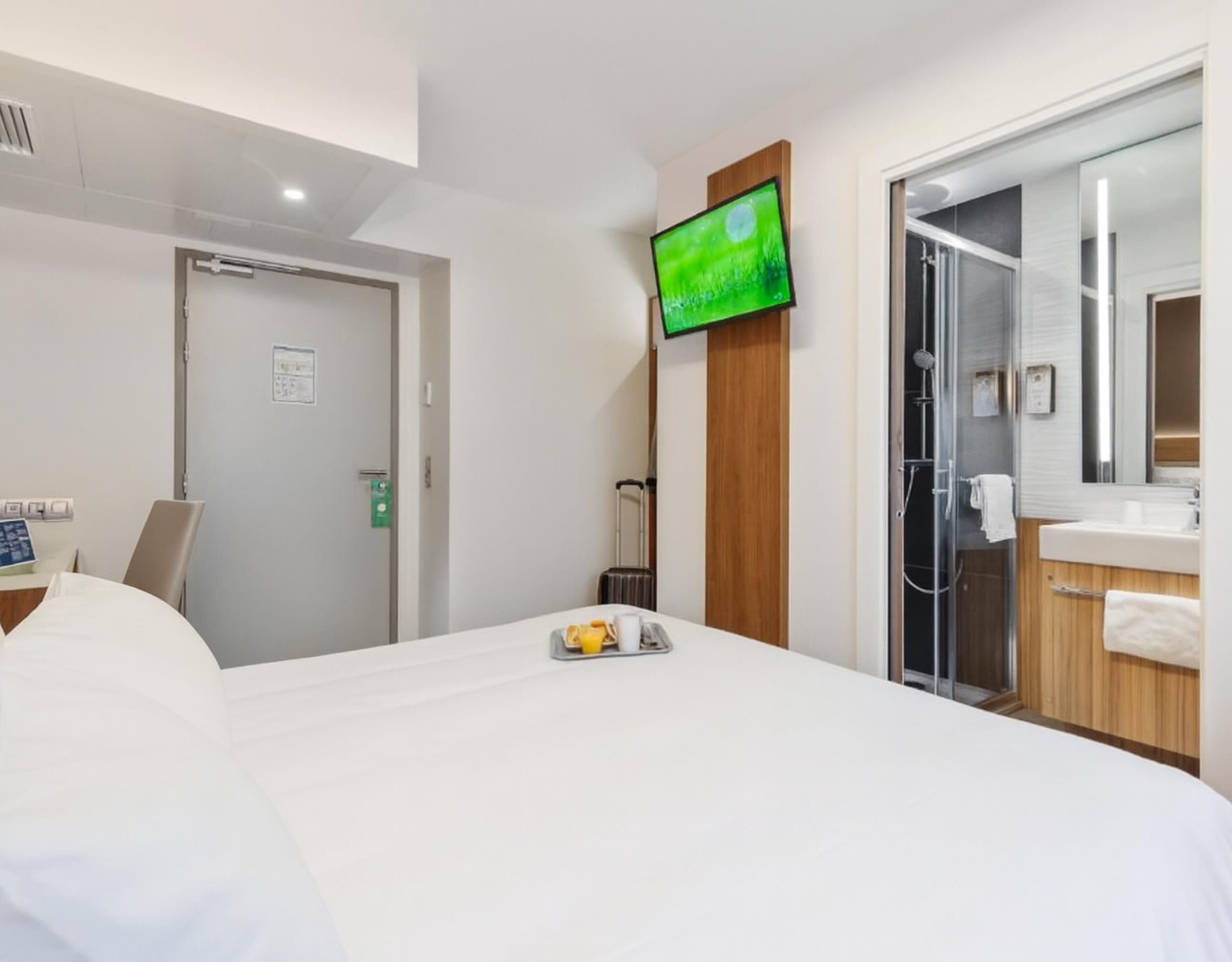 Quarto de hotel com cama, televisão, chuveiro e banheiro.