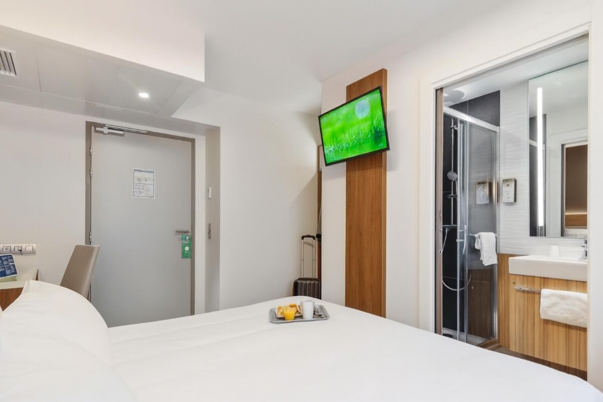 A hotel room with a bed, a TV, a shower, and a bathroom.