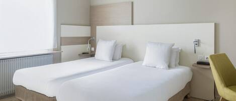 A hotel room with two beds, a bedside table, a chair, and a window with curtains.