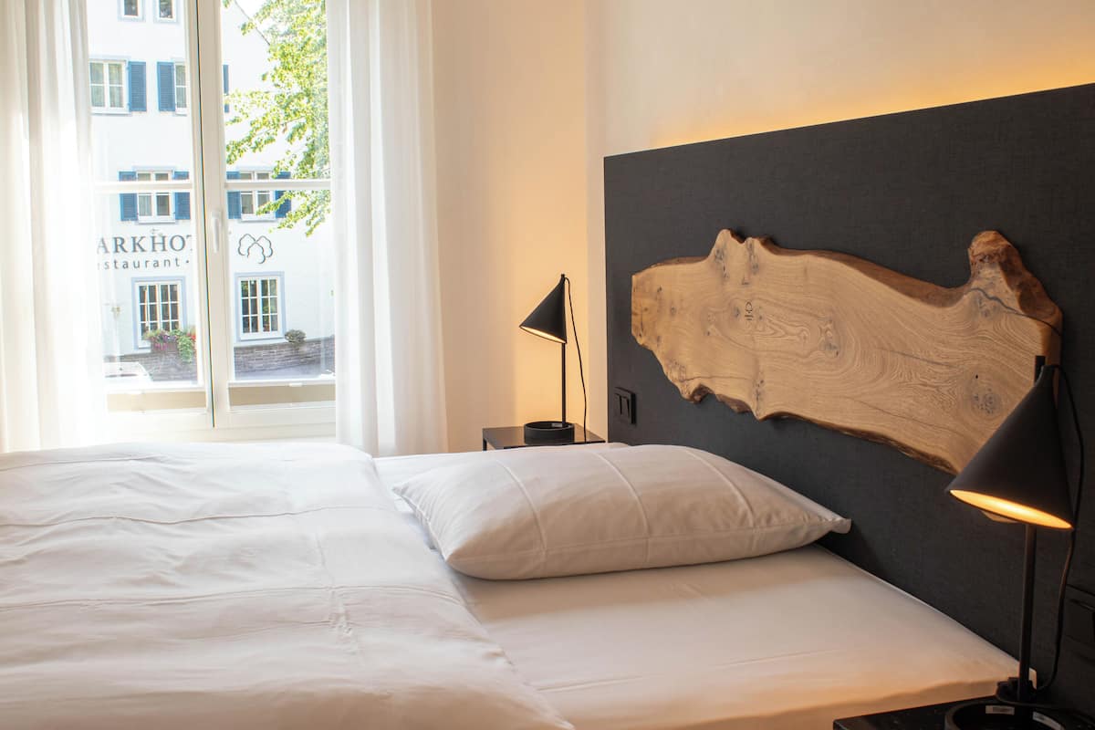 A hotel room with a bed, a nightstand, a lamp, and a large wooden headboard.