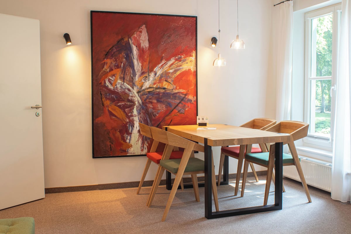 A dining area with a wooden table and chairs, a large abstract painting on the wall, and a window providing natural light.
