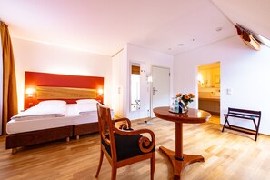 Ein Hotelzimmer mit einem Bett, einem Sessel, einem kleinen Tisch mit Blumenvase und einer Bank.