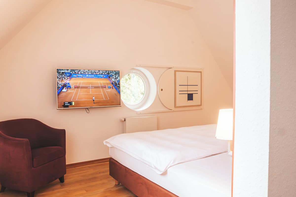 A bedroom with a bed, a chair, a TV mounted on the wall, and a window.