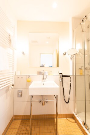 Ein Badezimmer mit einem weißen Waschbecken, einem Spiegel, einer Duschkabine aus Glas und einem gelben Seifenspender.