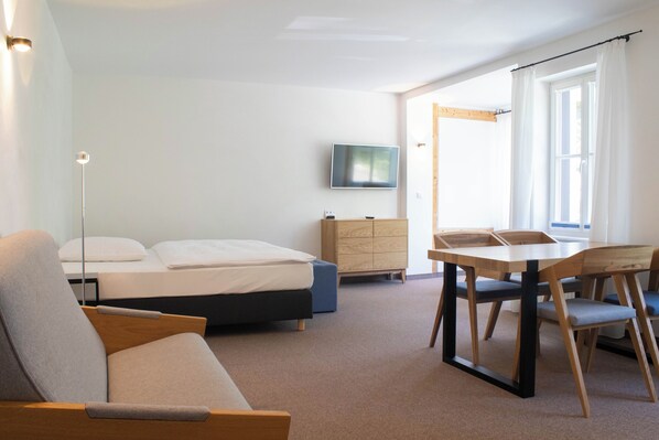 Una habitación de hotel moderna con cama, escritorio, silla, televisor y armario.