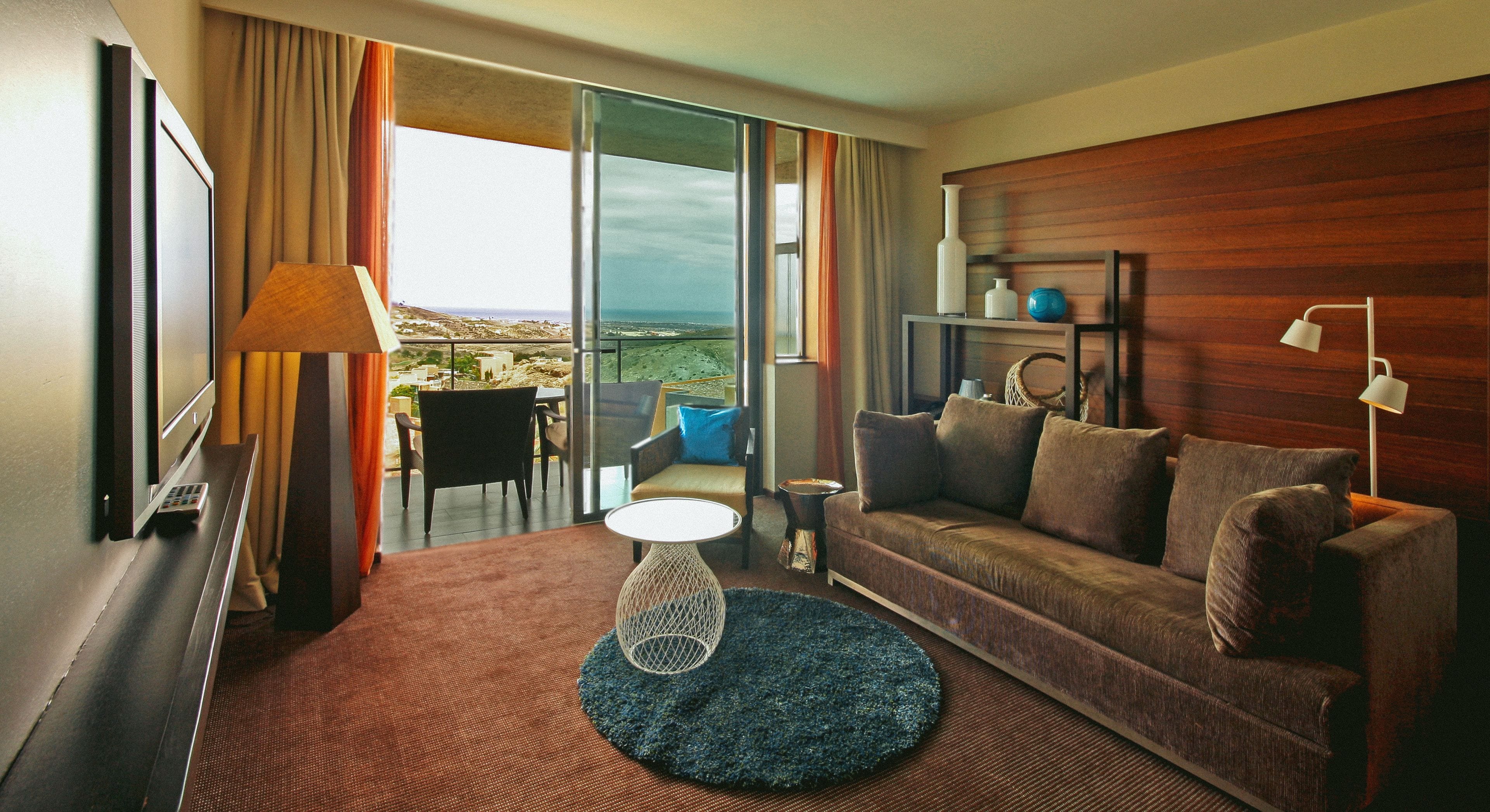 Habitación de hotel con sofá, una mesita, una lámpara y vistas al exterior.