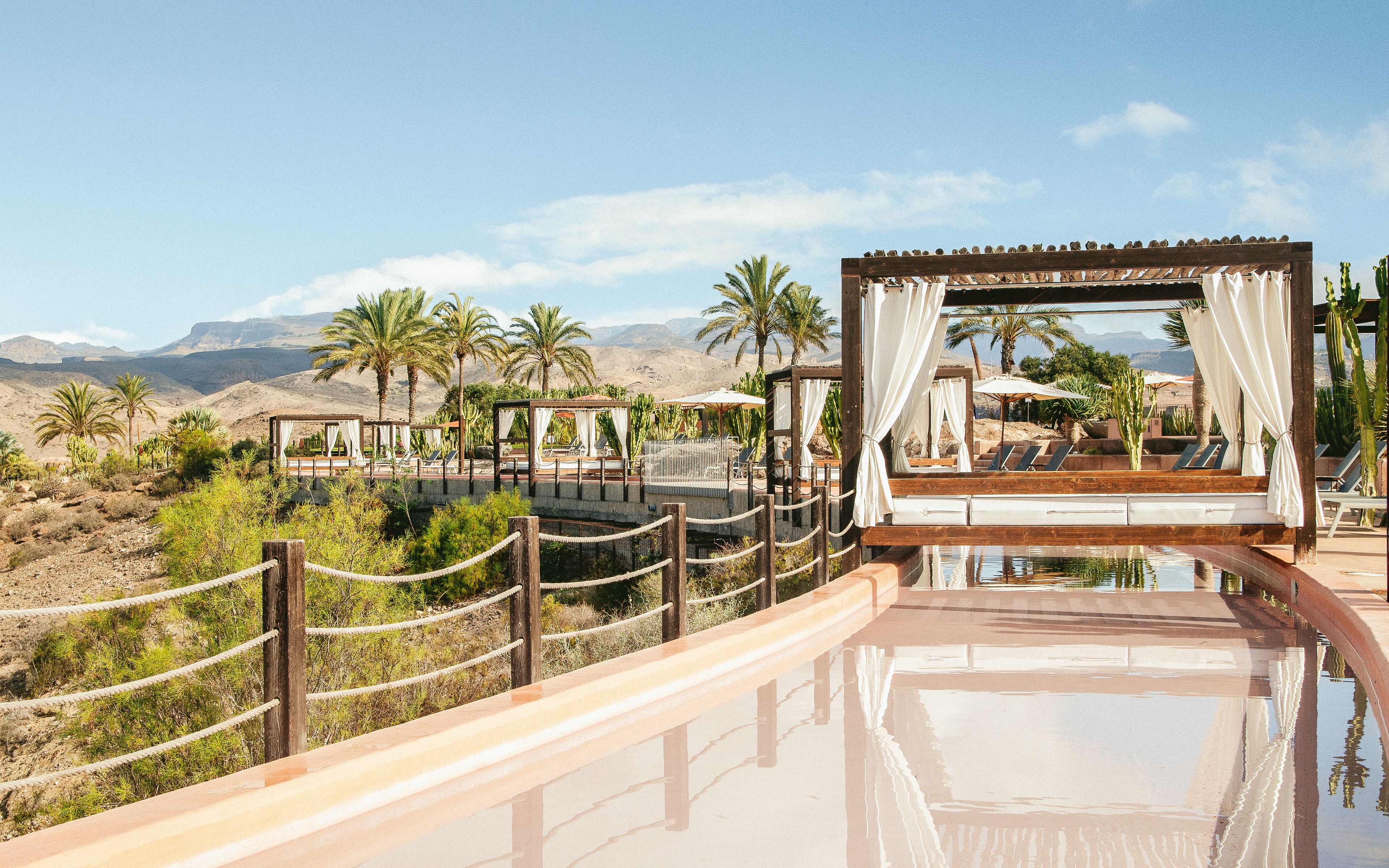 Ein Wüstenresort mit Pool, Strandkörben und Palmen.