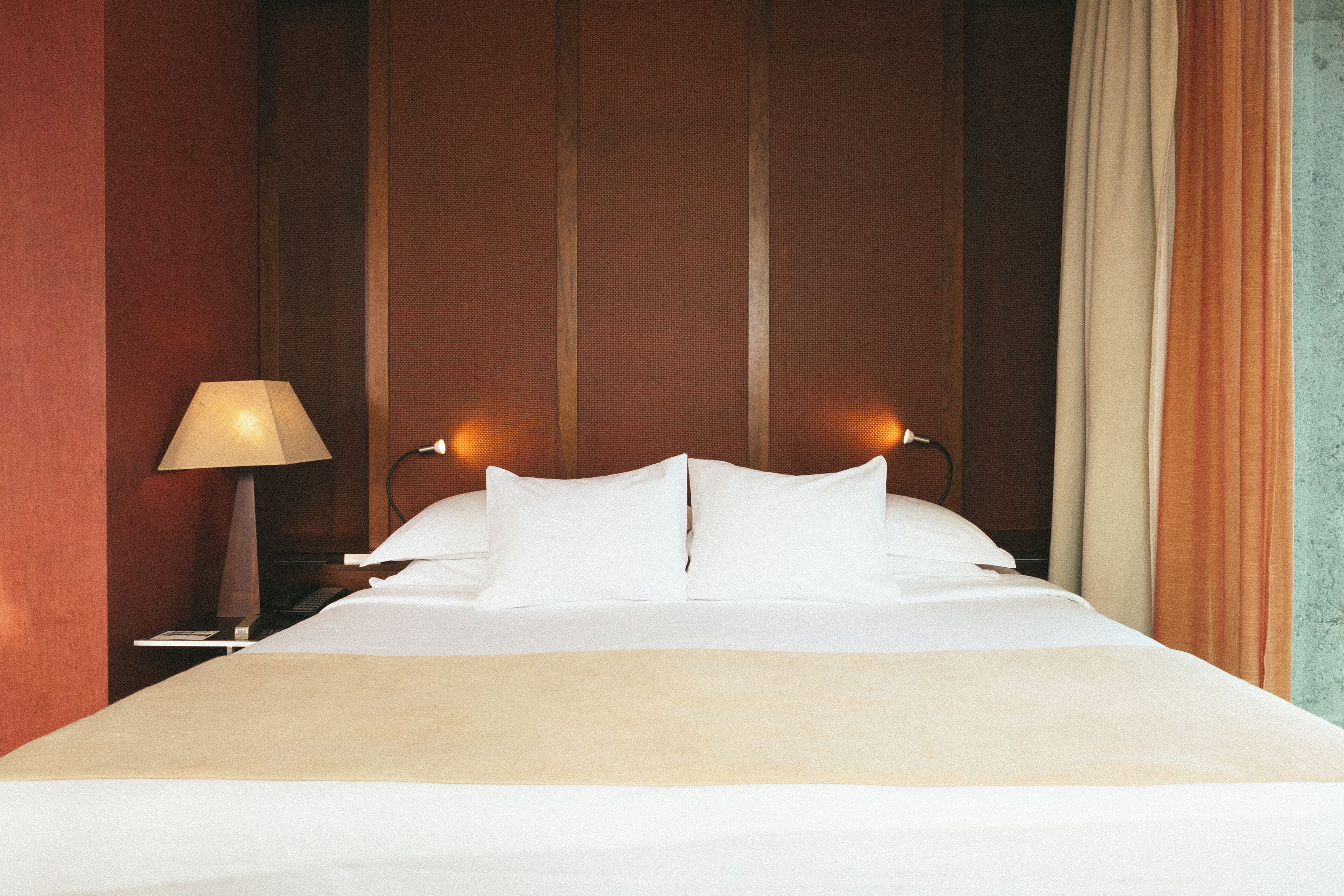 Una cama bien hecha con sábanas blancas, una lámpara de noche y un cabecero de madera.