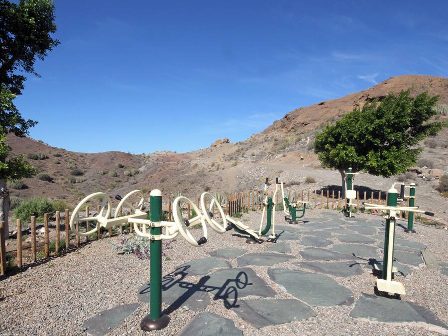 Zona de ejercicios al aire libre con bicicletas estáticas y una valla de madera.