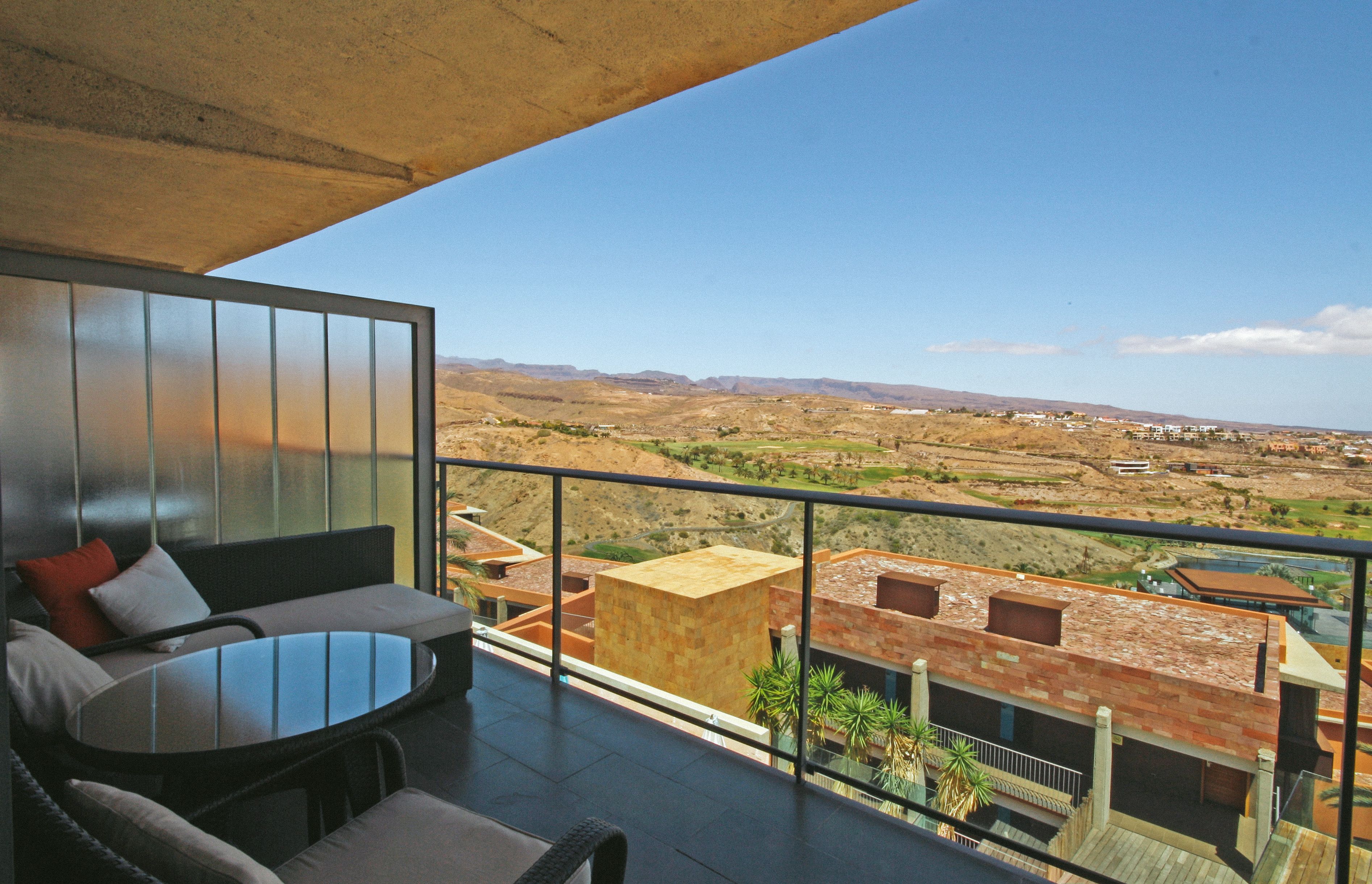 Un balcón con un sofá, una mesita y vistas a un paisaje montañoso.